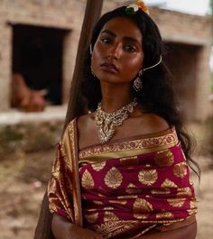 a woman in a red and gold sari standing next to a pole with her hands on her hips