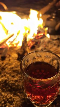 a glass filled with liquid sitting on top of a table next to a fire pit