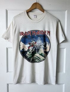 an iron maiden t - shirt hanging on a white door with a wooden hanger