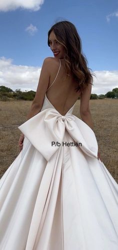 a woman in a white dress with a big bow on her back standing in a field