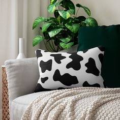 a black and white cow print pillow sitting on top of a couch next to a potted plant