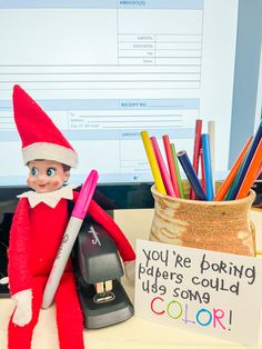 an elf is holding a pen and some colored pencils in front of a computer screen