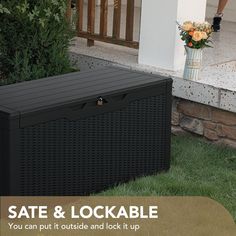 an outdoor storage box sitting in the grass next to a planter with flowers on it