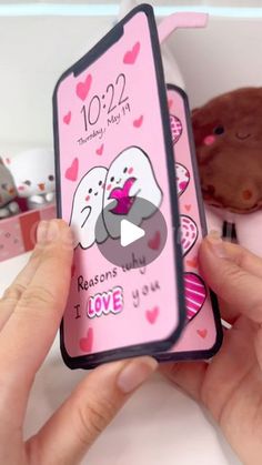 someone holding up a pink phone case with two dogs on it and hearts around the edges