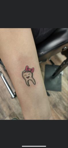 a woman's arm with a small tattoo of a tooth and bow on it