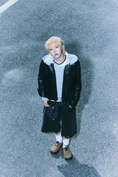 a young boy standing in the middle of an empty parking lot wearing a black jacket and white t - shirt