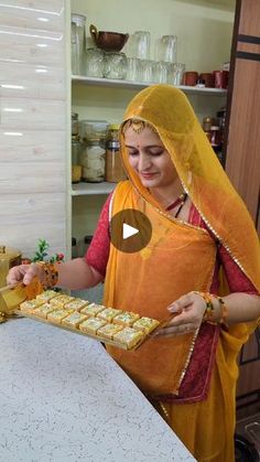 a woman in an orange and yellow sari is holding a tray with food on it