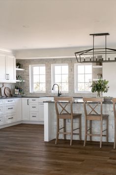 a kitchen with wooden floors and white cabinets, an island countertop and bar stools