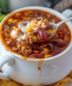 a spoon full of chili and corn soup on top of a white bowl with a yellow napkin