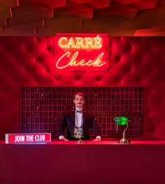 a man sitting at a desk in front of a neon sign that reads carre check