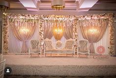 a stage set up for a wedding with white chairs and flowers on the wall behind it