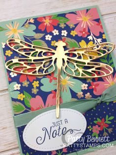 a close up of a card with a dragonfly on the front and flowers in the back