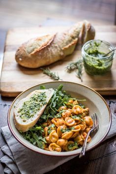 a bowl filled with pasta and greens next to bread