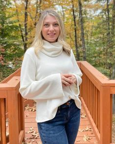 a woman standing on a wooden bridge in front of some trees with leaves around her