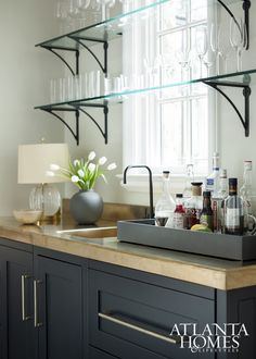 a kitchen counter with wine glasses and bottles on the shelf above it, next to a window