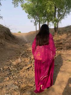 a woman in a pink dress walking down a dirt road