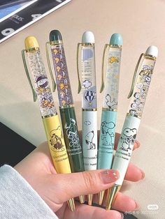 a person holding five pens in their hand with cartoon characters on them, all lined up together