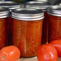 tomatoes and other vegetables sit in jars on a table