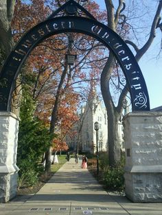 the entrance to an university campus with trees and people walking on the sidewalk in front