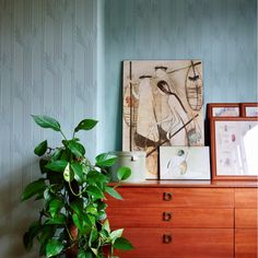 a potted plant sitting on top of a wooden dresser next to a framed painting