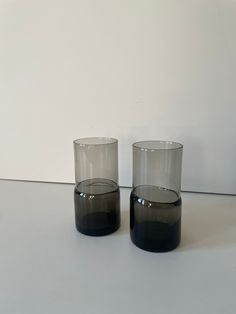 two glasses sitting on top of a table next to each other, one black and the other gray