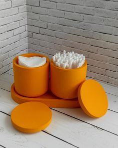 an orange container filled with toothbrushes on top of a white wooden table next to a brick wall