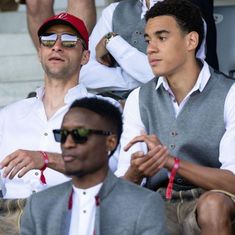 two men sitting next to each other in front of a crowd at a tennis match