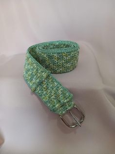 a green knitted belt with metal buckles on a white cloth covered tablecloth