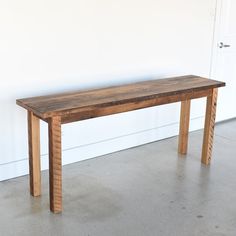 a wooden table sitting in front of a white wall with a door on it's side