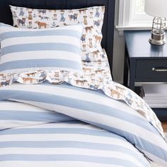 a bed with blue and white striped comforter next to a night stand on a wooden floor