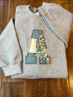 a gray sweatshirt with a patchwork letter on it