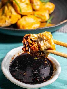 chopsticks holding up food over a bowl of dipping sauce on a blue table