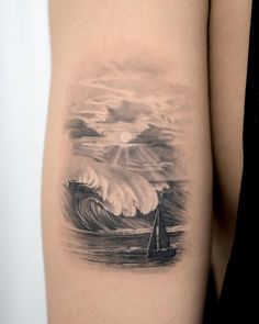 a woman's arm with a sailboat on the water and storm clouds in the background