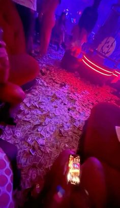 a person holding a cell phone in their hand while sitting on the floor covered with money