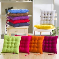 four different colored pillows stacked on top of each other in front of a white chair