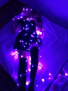 a woman laying on top of a bed covered in purple lights and black thigh high boots