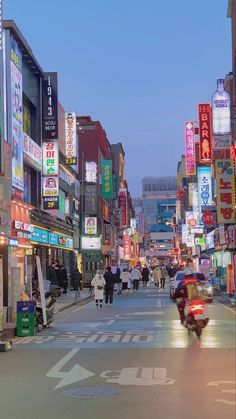 a busy city street filled with lots of neon signs and people walking down the sidewalk