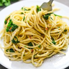 a white plate topped with pasta and spinach on top of a wooden table next to a fork