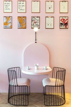 two chairs sitting at a table with cups on it in front of pink walls and framed pictures