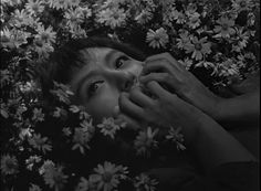 a woman is hiding in the flowers with her eyes open and hands on her face