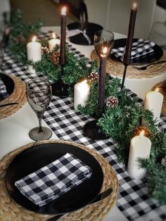 the table is set with black and white checkered linens, pine cones, candles, and evergreen branches