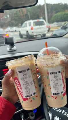 two people holding drinks in their hands while sitting in a car with other cars behind them