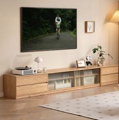 a man riding a bike down a street next to a wall mounted tv on top of a wooden cabinet