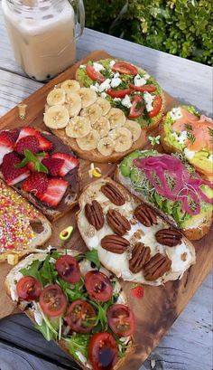 a wooden cutting board topped with sandwiches covered in fruit and veggies next to a glass of milk