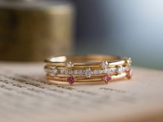 three gold rings with pink and white stones on top of a piece of parchment paper