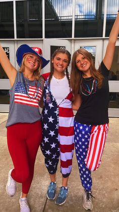 three girls in patriotic clothing posing for the camera with their arms up and one holding an american flag