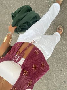 a woman with her legs crossed wearing white pants and a maroon sweater is standing in the street