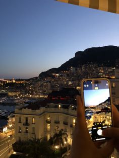 a person holding up a cell phone in front of a cityscape at night