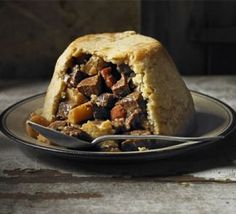 a piece of meat and potato pie on a black plate with a serving utensil