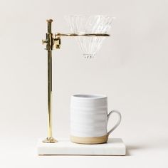 a coffee cup sitting on top of a white table next to a golden stand with a glass light